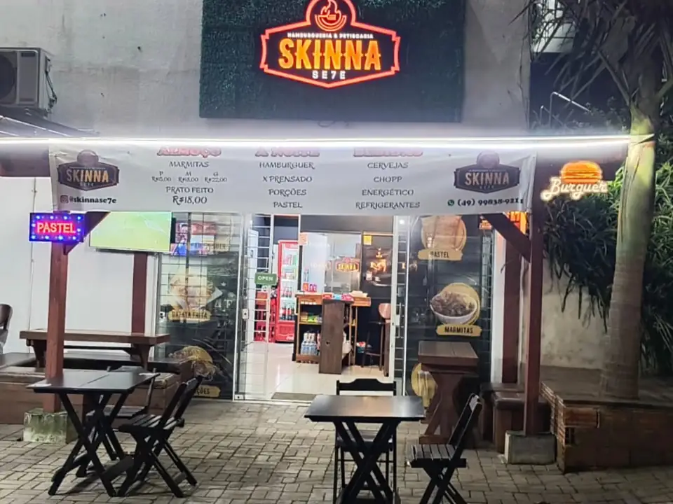 Fachada da Skinna Se7e à noite, com o letreiro aceso e mesas na calçada